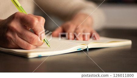 Side view of hand writing notes with pen in plain notebook. Minimalist workspace with natural lighting. Side view of hand writing notes with pen in plain notebook. Minimalist workspace with natural lighting. 126011800