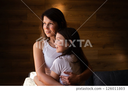 Adoptive mother holds her daughter close standing near window showing connection and warmth. Concept of modern family and power of love beyond biology. 126011803