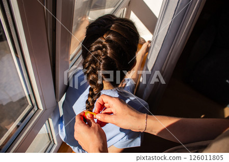 Mother braiding her daughter's hair, creating moment of love and connection. Childhood beauty, family bonding, and tender care. Image for parenting and family lifestyle themes. 126011805
