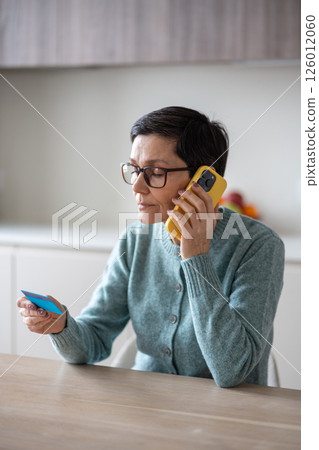 Trusting confused mature woman shares debit credit cvv details with unknown fraud caller at home Trusting confused mature woman shares debit credit cvv details with unknown fraud caller at home 126012060
