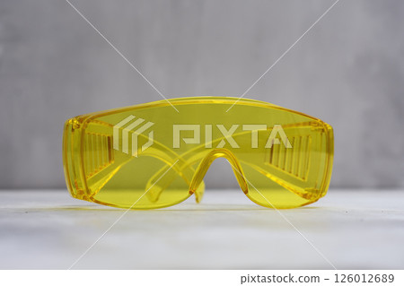 Bright yellow safety glasses placed on a light marble surface. Tool for eye protection during construction, laboratory work, or industrial tasks. Bright yellow safety glasses placed on a light marble surface. Tool for eye protection during construction, laboratory work, or industrial tasks. 126012689