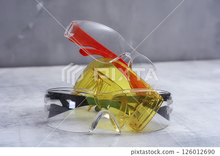 Set of protective safety glasses on a marble surface. Bright yellow lenses and clear lenses with red and green details. Concept for safety eye protection gear, and personal protective equipment. 126012690