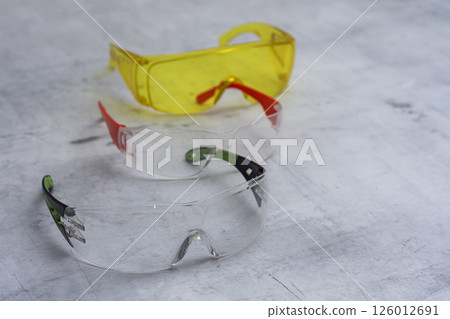 Set of protective safety glasses on a marble surface. Bright yellow lenses and clear lenses with red and green details. Concept for safety eye protection gear, and personal protective equipment. Set of protective safety glasses on a marble surface. Bright yellow lenses and clear lenses with red and green details. Concept for safety eye protection gear, and personal protective equipment. 126012691