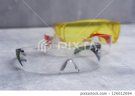 Set of protective safety glasses on a marble surface. Bright yellow lenses and clear lenses with red and green details. Concept for safety eye protection gear, and personal protective equipment. 126012694