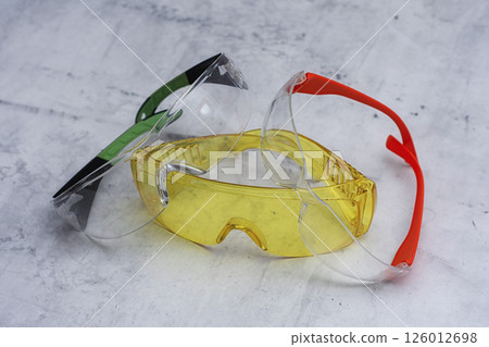 Set of protective safety glasses on a marble surface. Bright yellow lenses and clear lenses with red and green details. Concept for safety eye protection gear, and personal protective equipment. 126012698