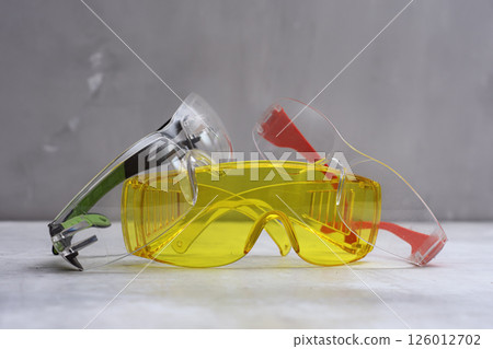 Set of protective safety glasses on a marble surface. Bright yellow lenses and clear lenses with red and green details. Concept for safety eye protection gear, and personal protective equipment. 126012702