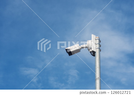 Outdoor CCTV camera on a metal pole against a clear blue sky. Outdoor CCTV camera on a metal pole against a clear blue sky. 126012721