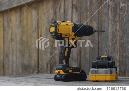 Yellow Cordless electric drill and battery charger on wooden background for DIY projects and repairs. Yellow Cordless electric drill and battery charger on wooden background for DIY projects and repairs. 126012768