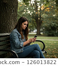 A woman looking at a smartphone on a park bench 126013822