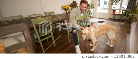 Close up portrait of handsome young man waiting for his order in coffee shop, petting a dog, resting in pet-friendly cafe 126013902