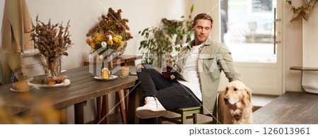Portrait of handsome young man sits in cafe with his dog, petting golden retriever, reading news on tablet, relaxing with cup of coffee Portrait of handsome young man sits in cafe with his dog, petting golden retriever, reading news on tablet, relaxing with cup of coffee 126013961
