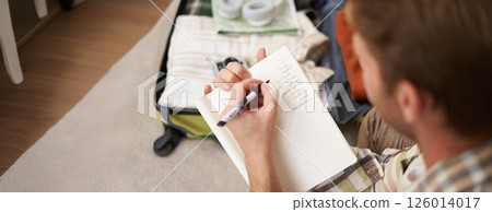 Close up portrait of man going through check-list, packing for holiday, looking at items he wants to bring on vacation Close up portrait of man going through check-list, packing for holiday, looking at items he wants to bring on vacation 126014017