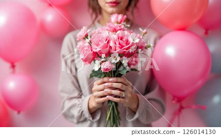 A woman proudly displays a bouquet of pink rose on a pink backdrop, symbolizing strength on International Women's Day 126014130