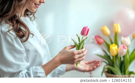Woman holding a vibrant bouquet of tulips against a soft white background, celebrating International Women's day 126014131