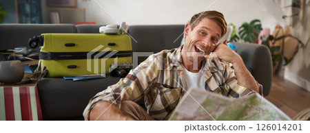 Portrait of handsome smiling young man, tourist shows call me gesture, phone hand, holding travel map, inviting to go on holiday, packed suitcase 126014201