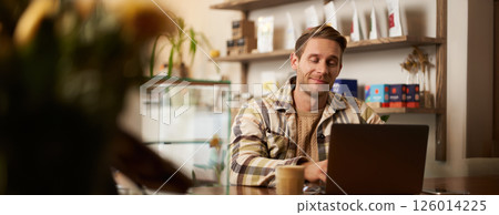 Portrait of handsome young digital nomad, man working in cafe on laptop, looking happy and pleased with his online project, sitting in co-working coffee shop Portrait of handsome young digital nomad, man working in cafe on laptop, looking happy and pleased with his online project, sitting in co-working coffee shop 126014225