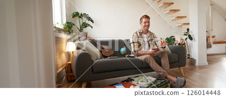 Portrait of smiling man with suitcase, looks at his notes in notebook, checks list of items for holiday 126014448