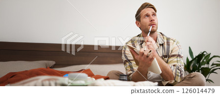 Portrait of thoughtful young man, tourist going on vacation, going through holiday check-list, writing down what he wants to take on travelling 126014479