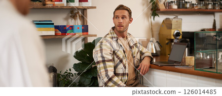 Small business concept. Handsome businessman, cafe owner, sitting near counter with laptop and smartphone, working in coffee shop 126014485