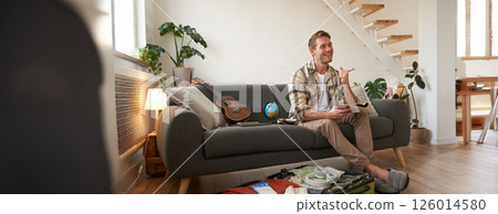 Portrait of young musician, tourist plans his next journey, holds pen and paper, creates check list of items to take on holiday, packs suitcase for vacation 126014580