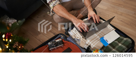 Close up shot of man, male hands using laptop on top of opened suitcase, packing for a holiday, going on vacation, prepare camera, two flight tickets for a trip abroad Close up shot of man, male hands using laptop on top of opened suitcase, packing for a holiday, going on vacation, prepare camera, two flight tickets for a trip abroad 126014595