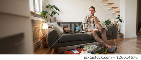 Portrait of young man packing for a trip, going on vacation, putting clothes inside suitcase, preparing for holiday 126014676