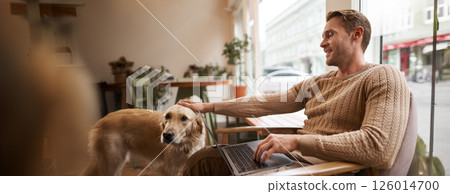 Portrait of young man, digital nomad, sitting in cafe near window, using laptop, working with his pet, petting golden retriever while sitting in chair with computer on laps Portrait of young man, digital nomad, sitting in cafe near window, using laptop, working with his pet, petting golden retriever while sitting in chair with computer on laps 126014700