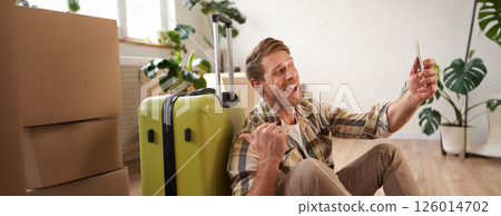Cheerful smiling man with suitcase, video chats using smartphone, takes selfie, goes on holiday 126014702