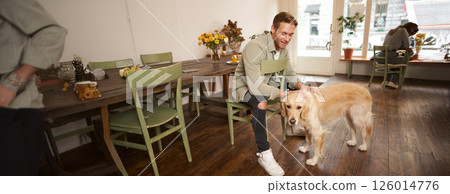 Lifestyle portrait of handsome smiling man sitting in pet friendly cafe with his beautiful dog, petting golden retriever, waiting for an order 126014776