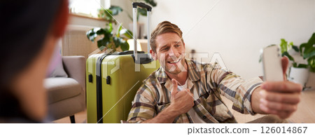 Smiling man with suitcase, takes selfies on mobile phone, shares photos on social media, going on holiday, travelling Smiling man with suitcase, takes selfies on mobile phone, shares photos on social media, going on holiday, travelling 126014867