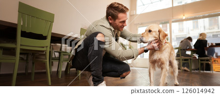 Close up portrait of handsome happy man petting his cute dog in a pet-friendly cafe. Coffee shop visitor with his golden retriever Close up portrait of handsome happy man petting his cute dog in a pet-friendly cafe. Coffee shop visitor with his golden retriever 126014942