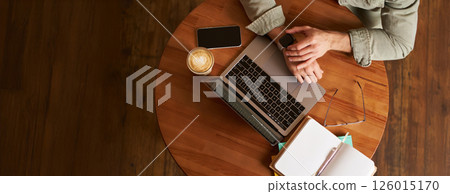 Top view of male hands, man checking time or message on his digital watch, sitting in a cafe with laptop, mobile phone and notebook, drinking coffee Top view of male hands, man checking time or message on his digital watch, sitting in a cafe with laptop, mobile phone and notebook, drinking coffee 126015170