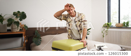 Portrait of man struggling to close suitcase full of clothes, putting effort to pack luggage for holiday, going on long vacation with lots of things 126015300