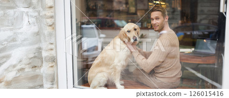 Outdoor shot of a pet-friendly cafe where man sits near the window with his fluffy golden retriever and smiles at camera. Coffee shop visitor with a dog Outdoor shot of a pet-friendly cafe where man sits near the window with his fluffy golden retriever and smiles at camera. Coffee shop visitor with a dog 126015416