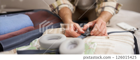 Close up of male hands, man fastening clothes inside suitcase, packing his belongings in luggage, going on holiday, travelling 126015425