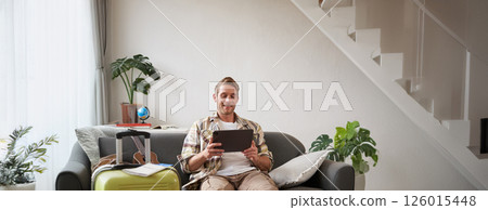 Vertical shot of man, tourist with suitcase, looking at digital tablet, reading about travel destination, booking hotel on gadget 126015448