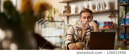 Portrait of man looking disappointed at laptop screen, working remotely, freelancer sitting in cafe, drinking coffee, reading message on monitor with unamused, upset face 126015488