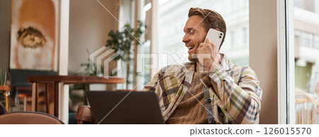 Image of happy cafe visitor, man with laptop, calling a friend over the phone. Businessman talking on telephone, working online from coffee shop, laughing and smiling 126015570