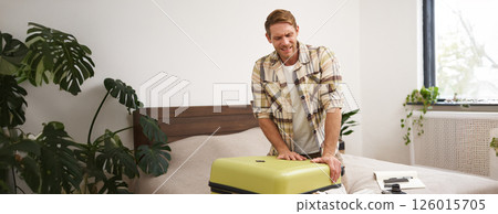Image of young traveller, tourist struggling to shut his suitcase, pushing on luggage to close it, carry a lot of clothes on vacation Image of young traveller, tourist struggling to shut his suitcase, pushing on luggage to close it, carry a lot of clothes on vacation 126015705