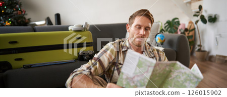 Portrait of handsome young man, traveller with suitcase, looking at paper map, choosing where to go on vacation, going on holiday, choosing route Portrait of handsome young man, traveller with suitcase, looking at paper map, choosing where to go on vacation, going on holiday, choosing route 126015902