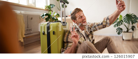 Portrait of smiling handsome man with suitcase, taking selfie with luggage, posting on social media about going on holiday 126015907