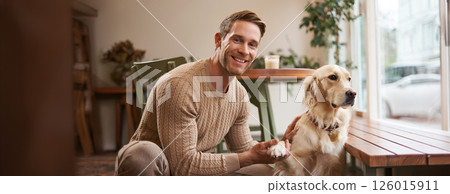 Portrait of young handsome dog-owner, spending time with his pet in a cafe, sitting indoors, looking outside window Portrait of young handsome dog-owner, spending time with his pet in a cafe, sitting indoors, looking outside window 126015911