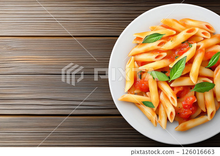 A plate of pasta topped with rich tomato sauce and fresh basil, served on a wooden table, showcasing a delightful and flavorful Italian meal. 126016663