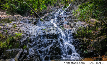 Serene Waterfall Cascading Over Jagged Rocks in a Forested Area 126016936