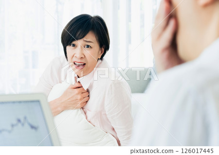 A middle-aged couple is shocked when looking at a computer in the living room A middle-aged couple is shocked when looking at a computer in the living room 126017445