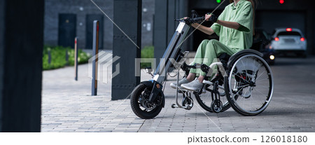 A faceless woman in a wheelchair with an assistive device for manual control. Electric handbike.  126018180