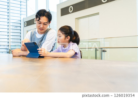 A girl looking at a tablet and a man teaching her how to use it A girl looking at a tablet and a man teaching her how to use it 126019354