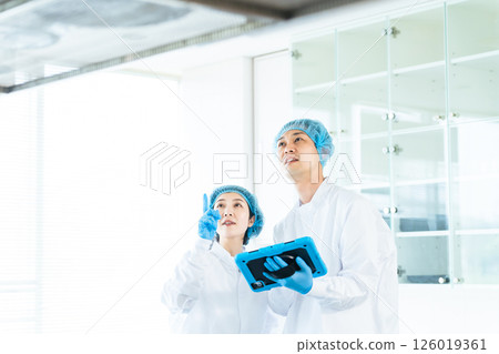 Male and female workers wearing sanitary white coats managing inventory in a food warehouse Male and female workers wearing sanitary white coats managing inventory in a food warehouse 126019361