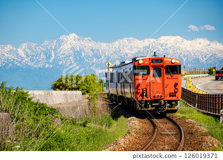 A JR Himi Line diesel train running along Amaharashi Coast with the overwhelming snow-capped Tateyama mountain range in the background A JR Himi Line diesel train running along Amaharashi Coast with the overwhelming snow-capped Tateyama mountain range in the background 126019371