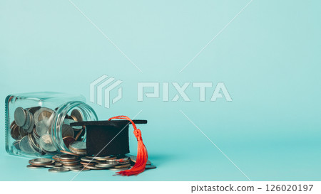 Coins in a glass jar and graduation cap on blue background. 126020197
